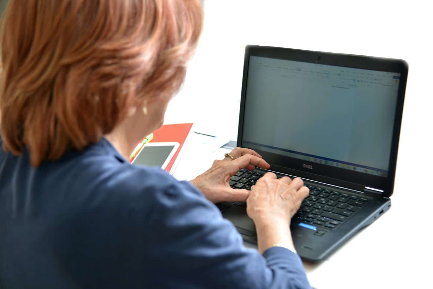 A person types on a laptop at a white desk.